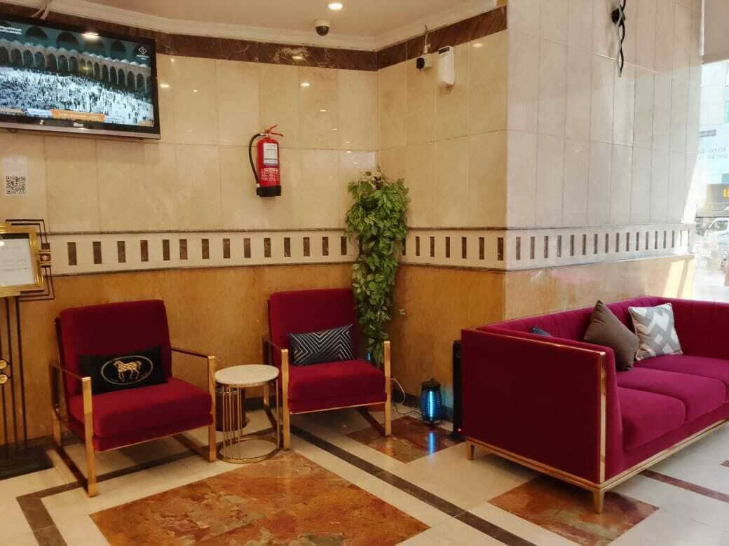 Un hall con dos sillones rojos, un sofá rojo, una mesita redonda y un televisor montado en la pared.