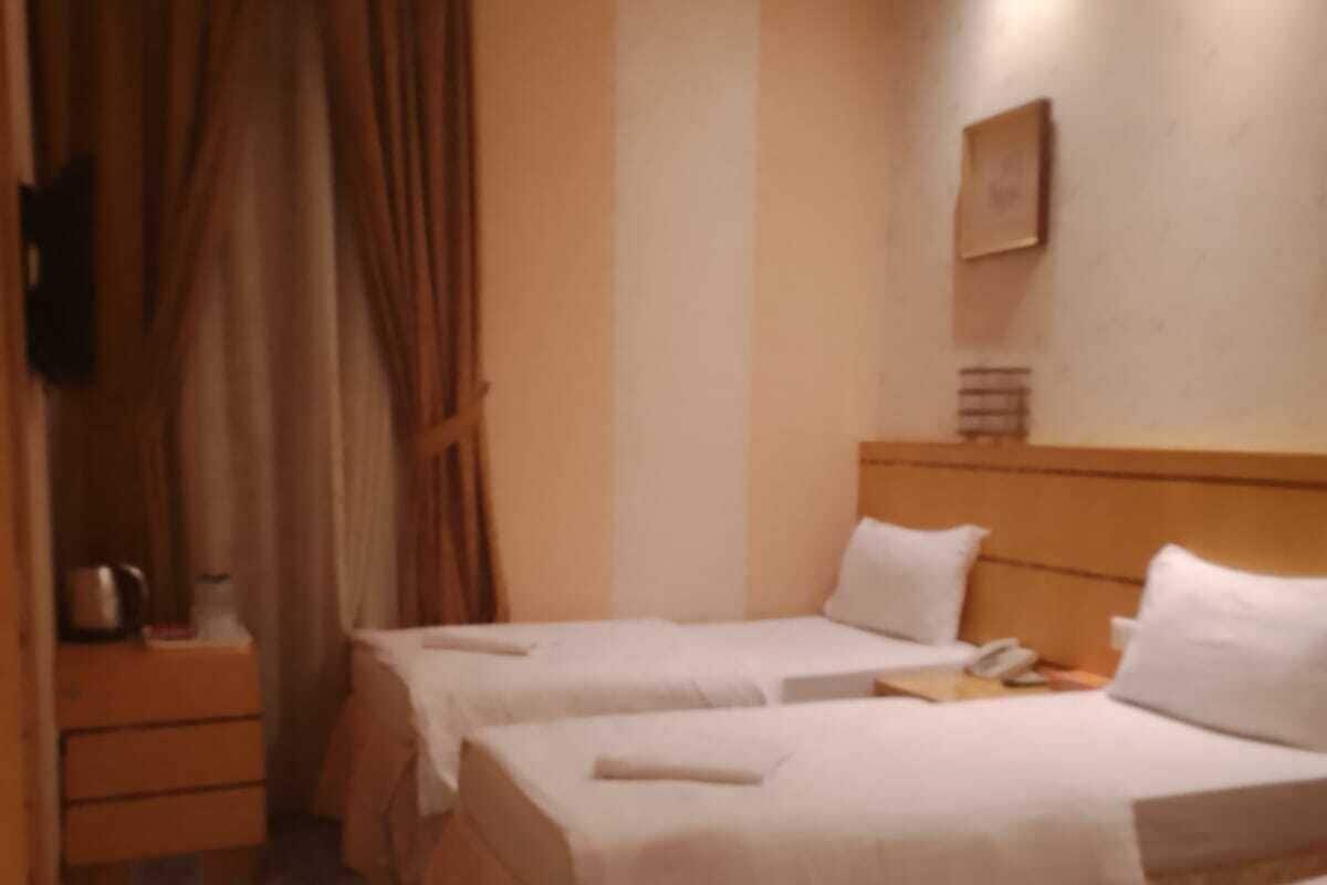 Une chambre d’hôtel avec deux lits, une table de chevet, une lampe et une fenêtre avec des rideaux.