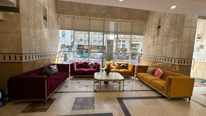 A spacious lobby with a marble floor, large windows offering a view of the city, and a mix of red and yellow sofas.