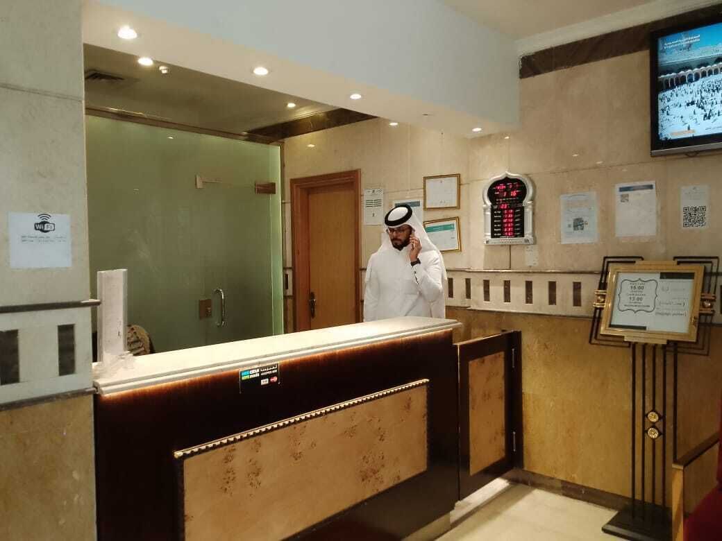 A reception desk with a digital display, a wooden counter, and a man in traditional attire standing behind it.