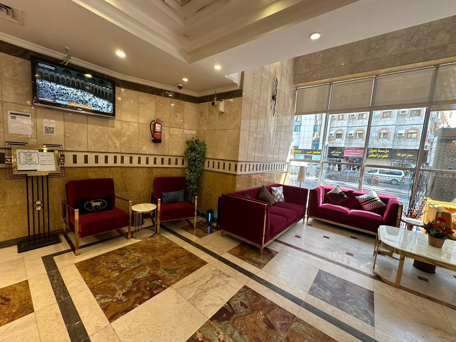 A lobby with red sofas, a TV mounted on the wall, a fire extinguisher, and a large window offering a view of the street.