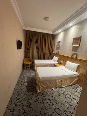 Habitación de hotel con dos camas, una silla, una mesita y una cortina.