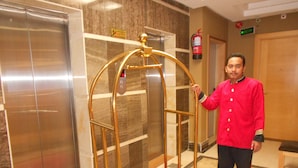 A man in a red jacket standing next to a golden elevator with a red carpet.