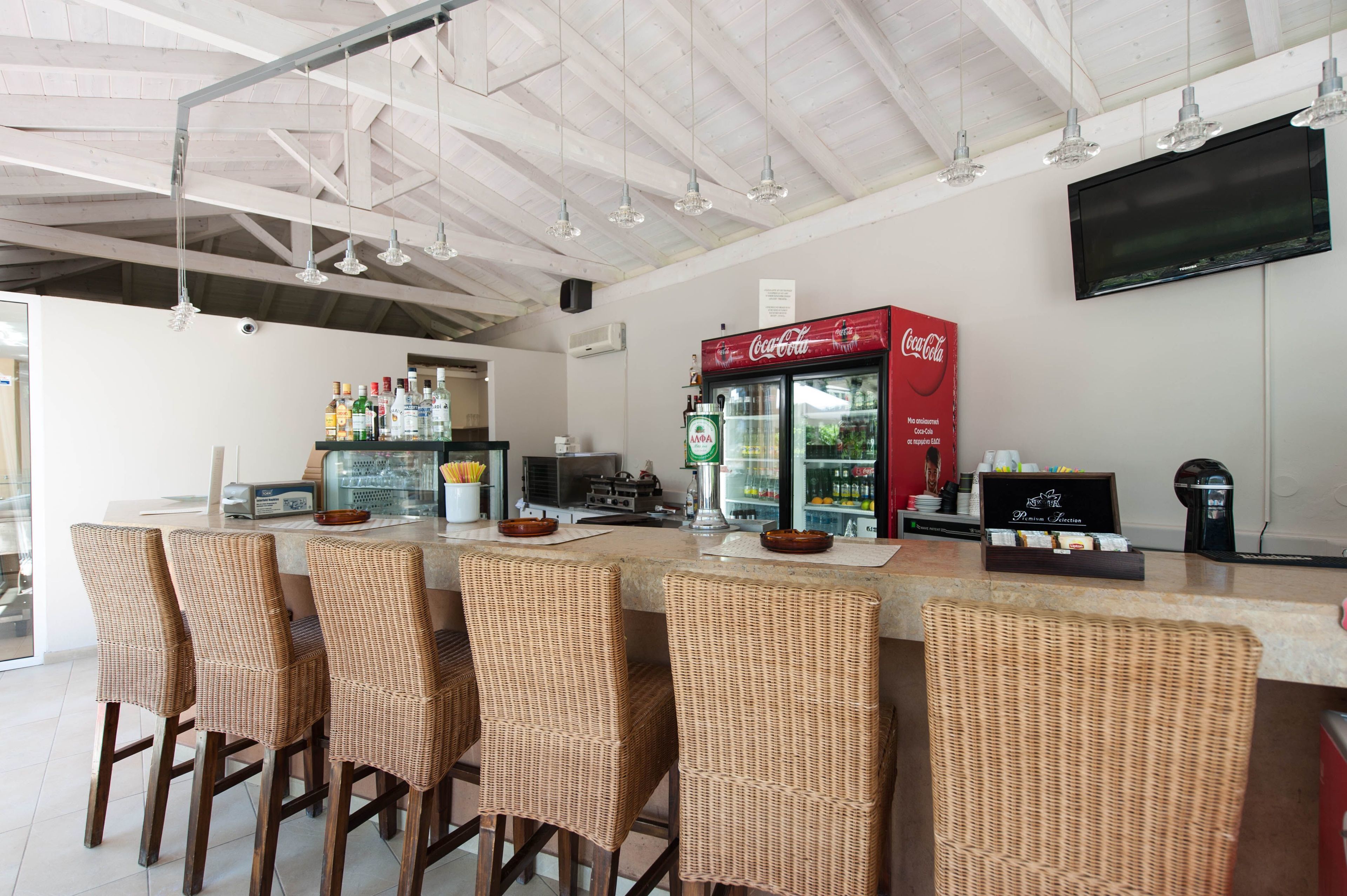 Zona de bar con sillas de mimbre, un refrigerador de Coca-Cola y un televisor de pantalla plana en la pared.