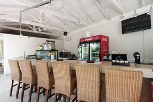Zona de bar con sillas de mimbre, un refrigerador de Coca-Cola y un televisor de pantalla plana en la pared.