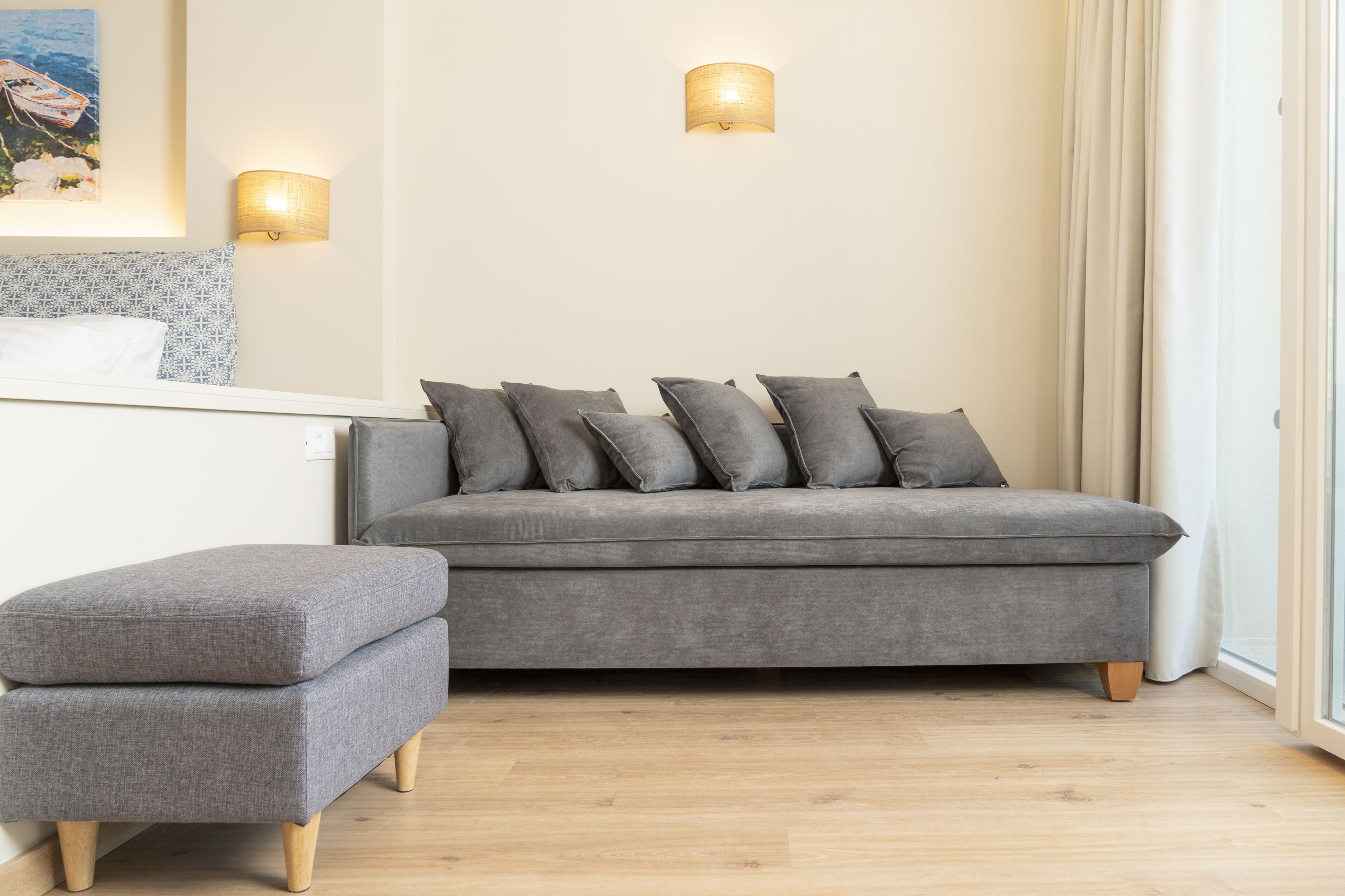 En grå sofa med mange puder, et matchende sk footmøbel og to vægmonterede lamper.