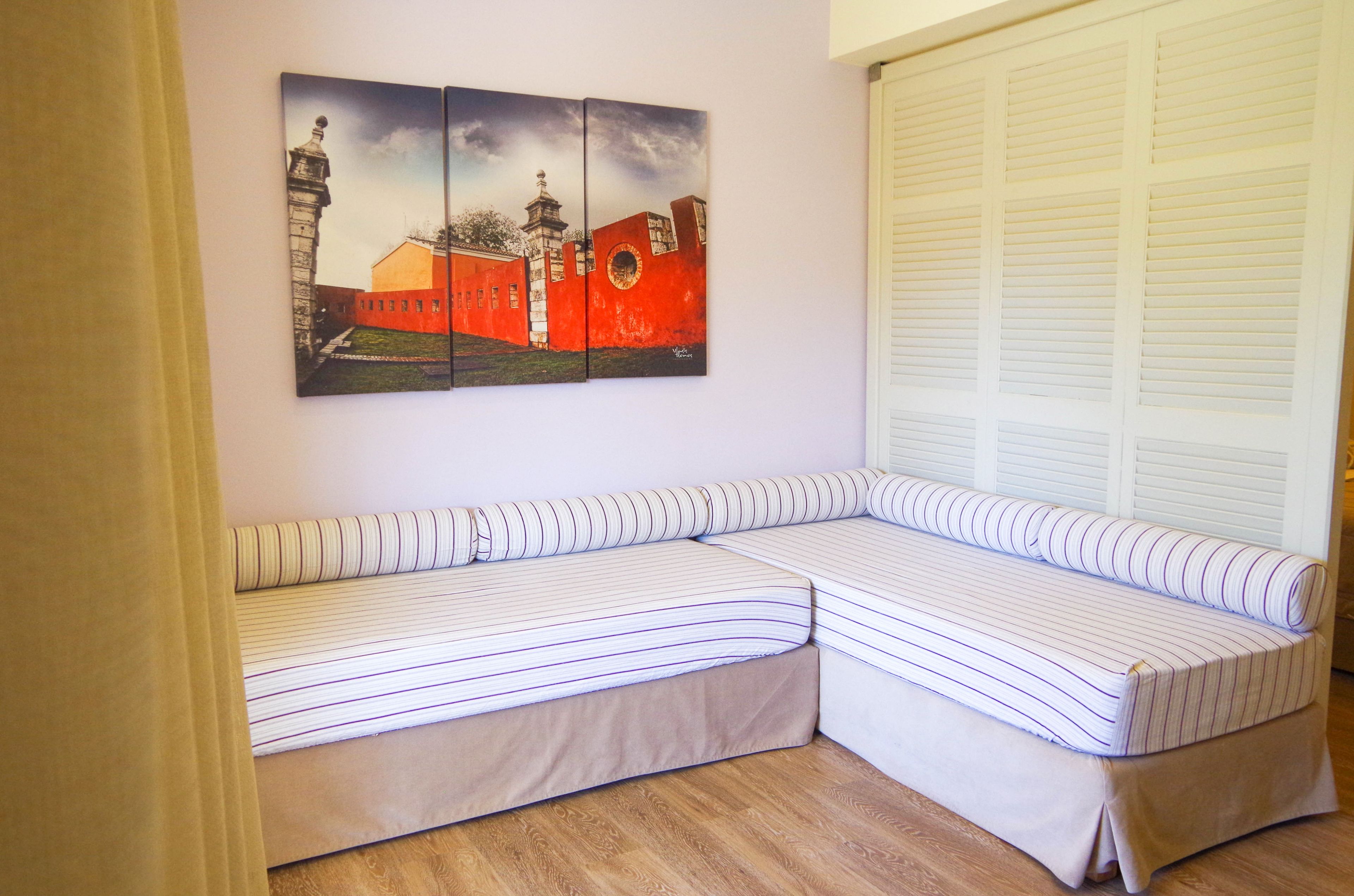 Ein Zimmer mit einer Ecksofa-Schlafgelegenheit, einem Bild eines Gebäudes und einem Fenster mit Jalousien.