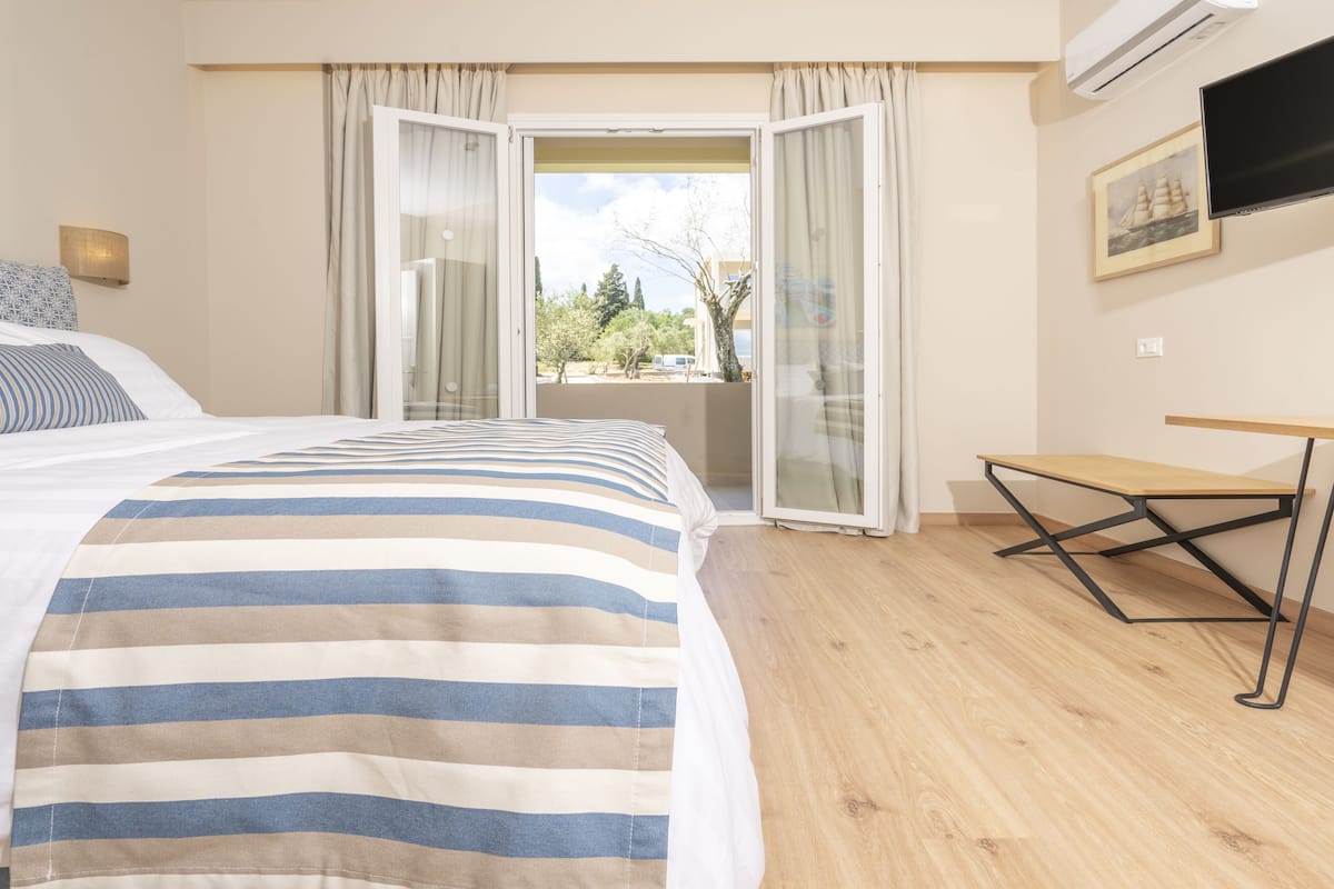 A hotel room with a bed, a desk, a window with curtains, and a painting on the wall.