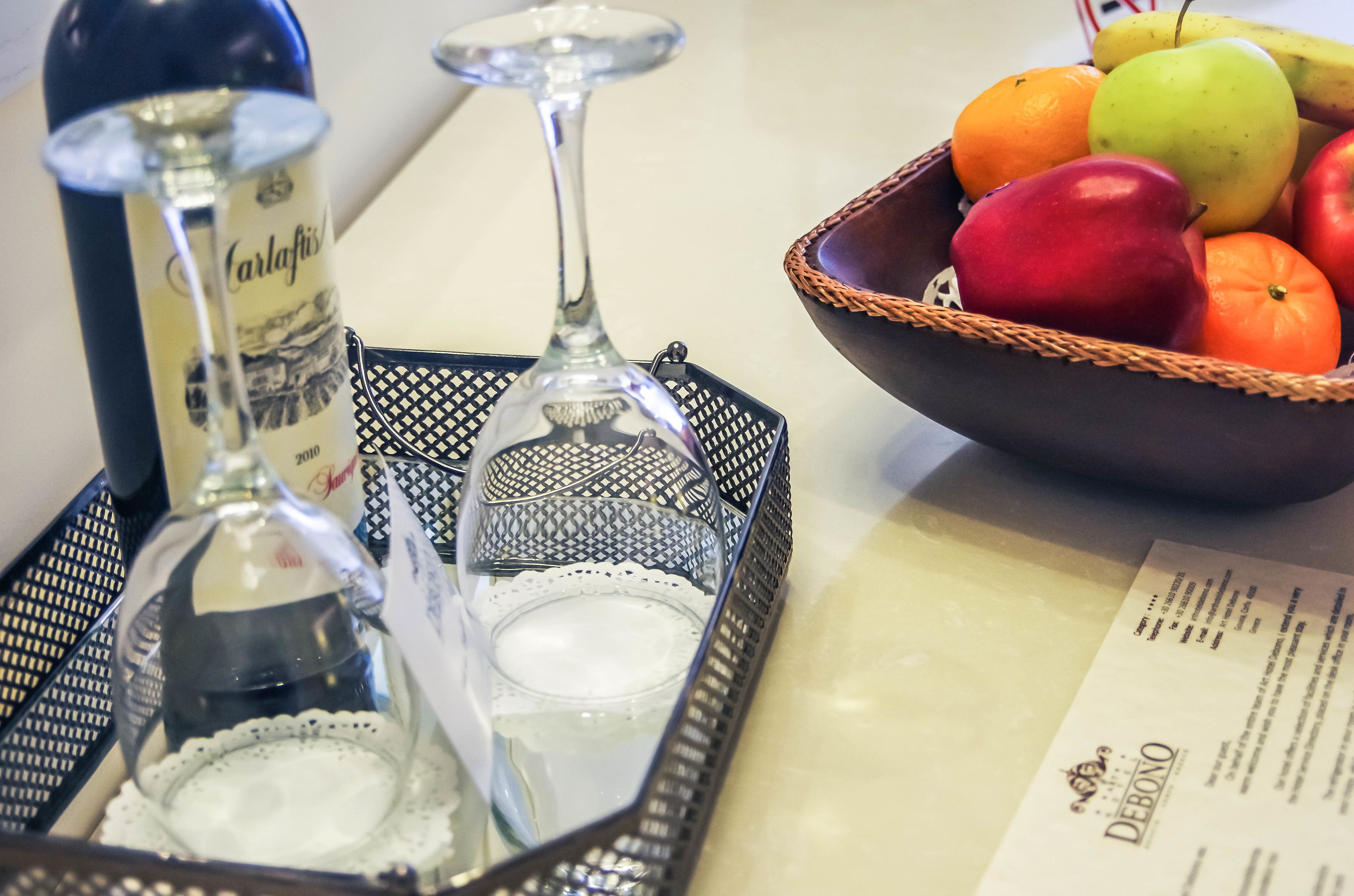 A tray with a bottle of Carlafis wine, two glasses, and a basket of fruit including apples and oranges.