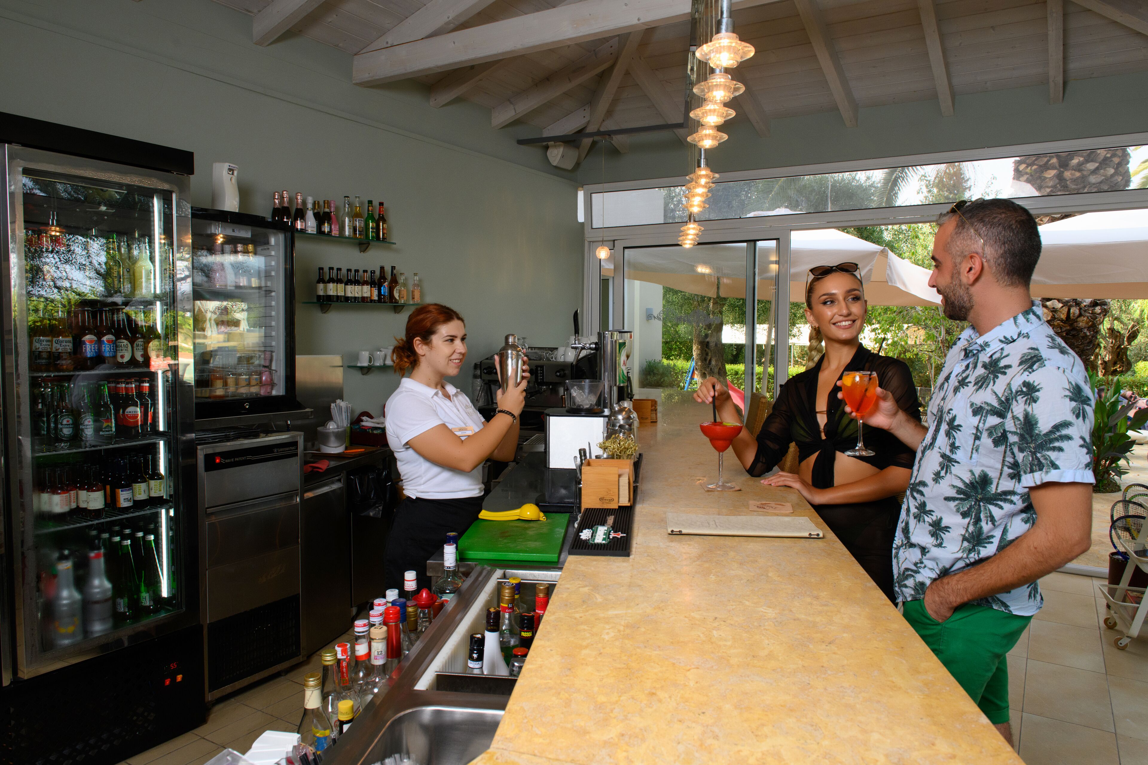 A bar area with a counter, a refrigerator stocked with bottles, and a view of the outdoors.
