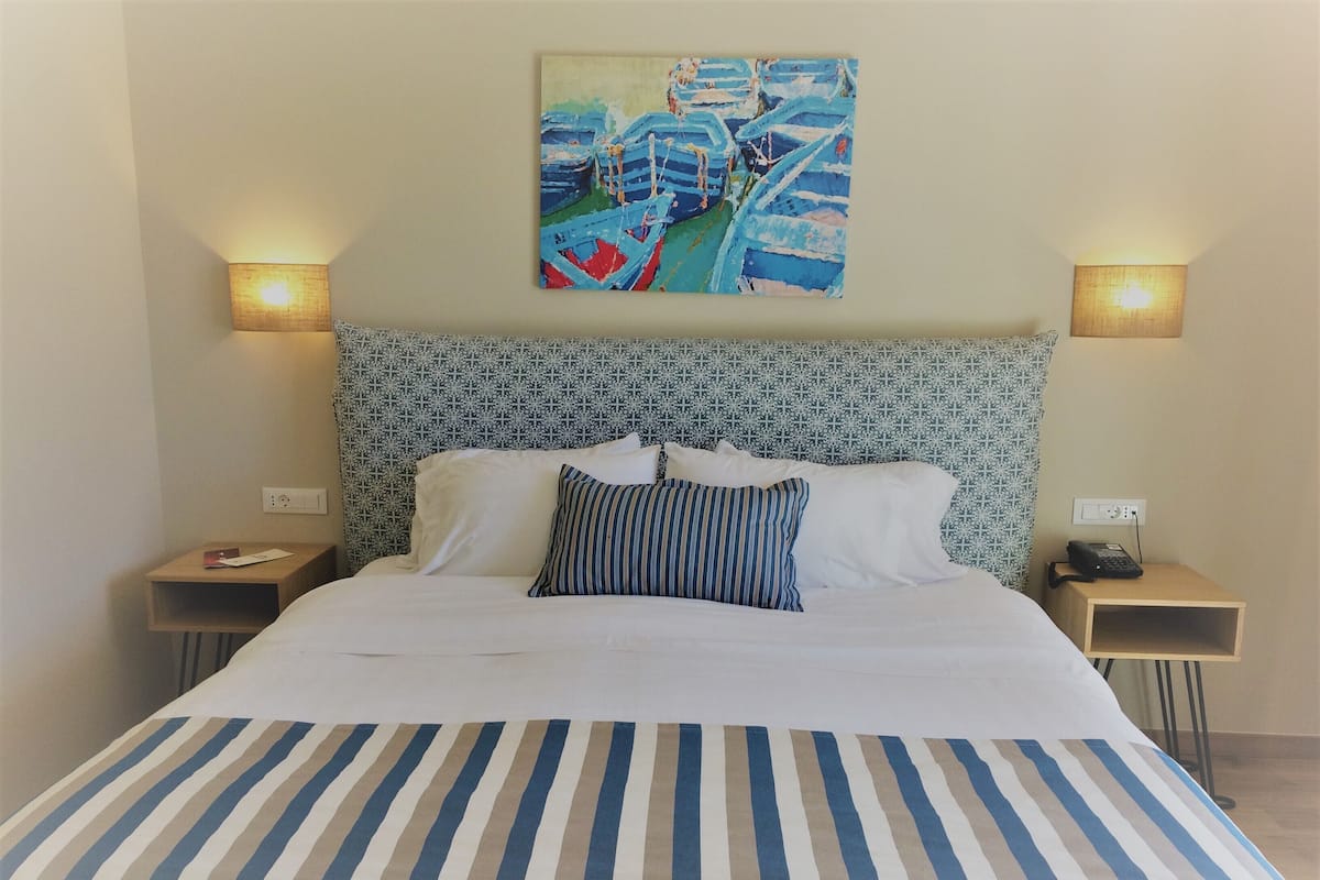 A hotel room with a bed, two bedside tables, a patterned headboard, and a painting on the wall.
