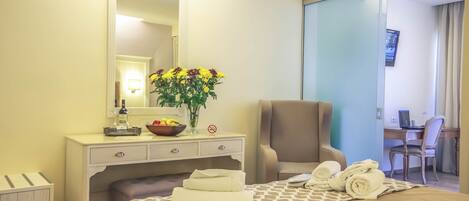A hotel room with a bed, a desk, a chair, a mirror, a vase with flowers, and towels.