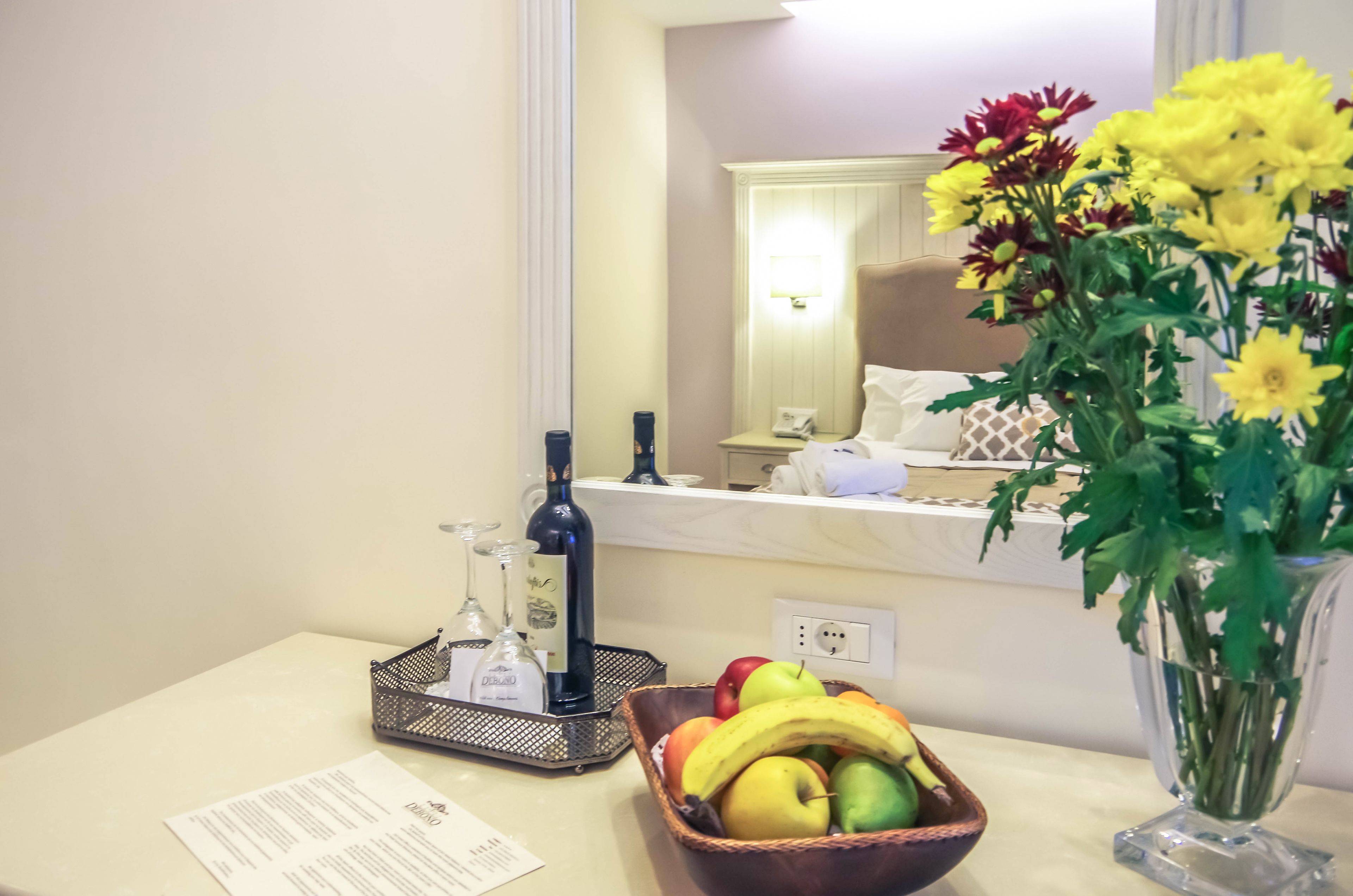 Ein Hotelzimmer mit Esstisch, Obstschale, Blumenvase und einer Minibar.