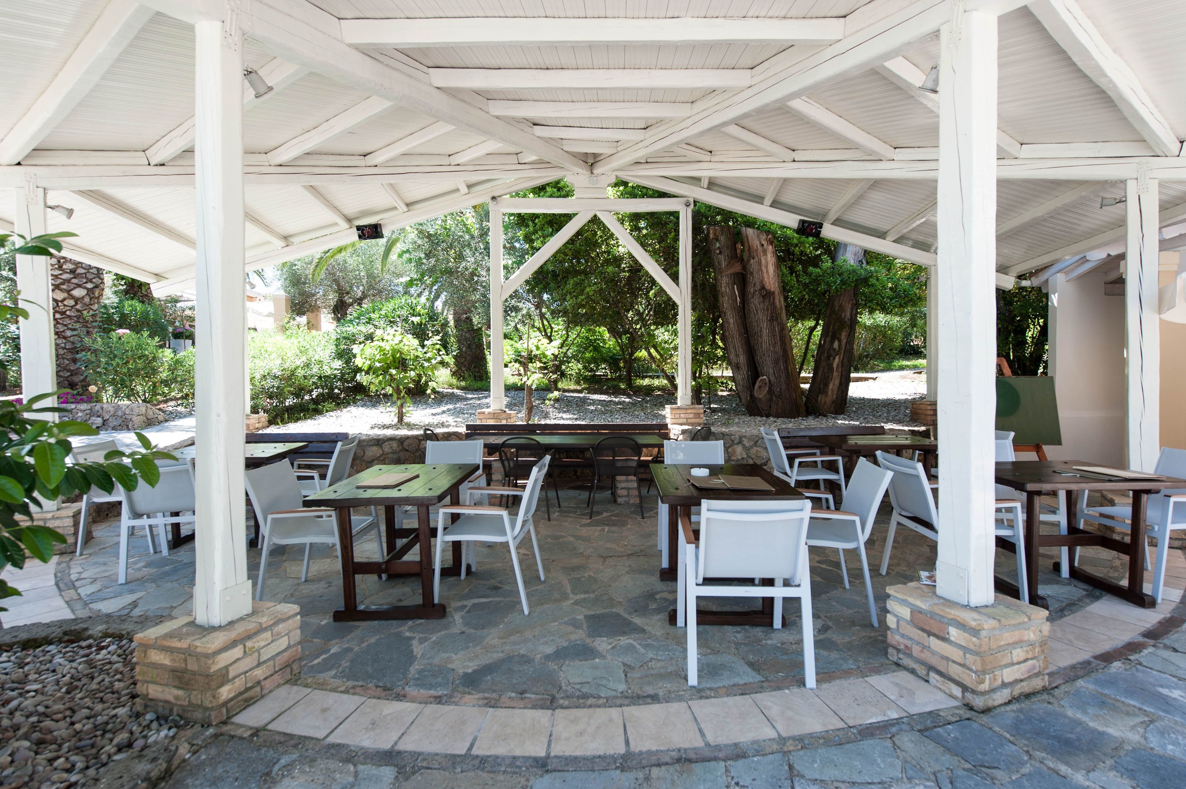 An outdoor patio with stone flooring, white chairs, and tables under a white pergola.
