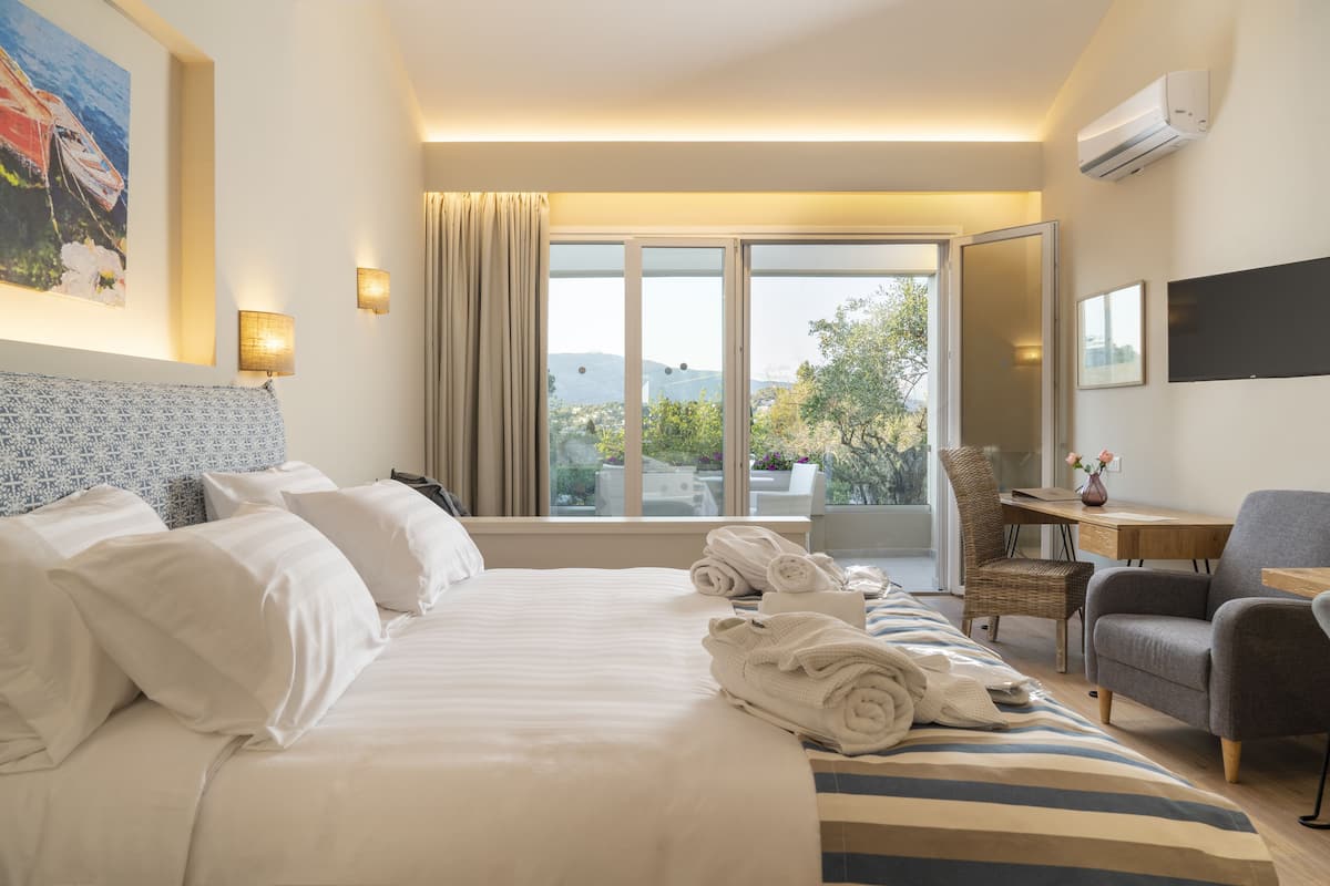 A hotel room with a large bed, a desk, a chair, and a view of the outdoors.