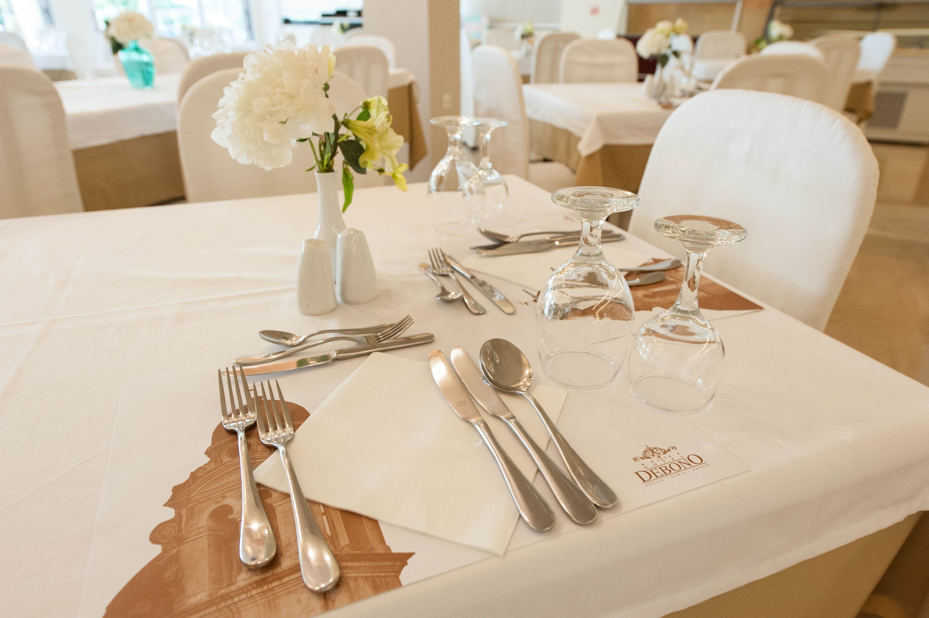 Een gedekte tafel voor een diner, met een witte tafelkleed, bestek en een glazen karaf.