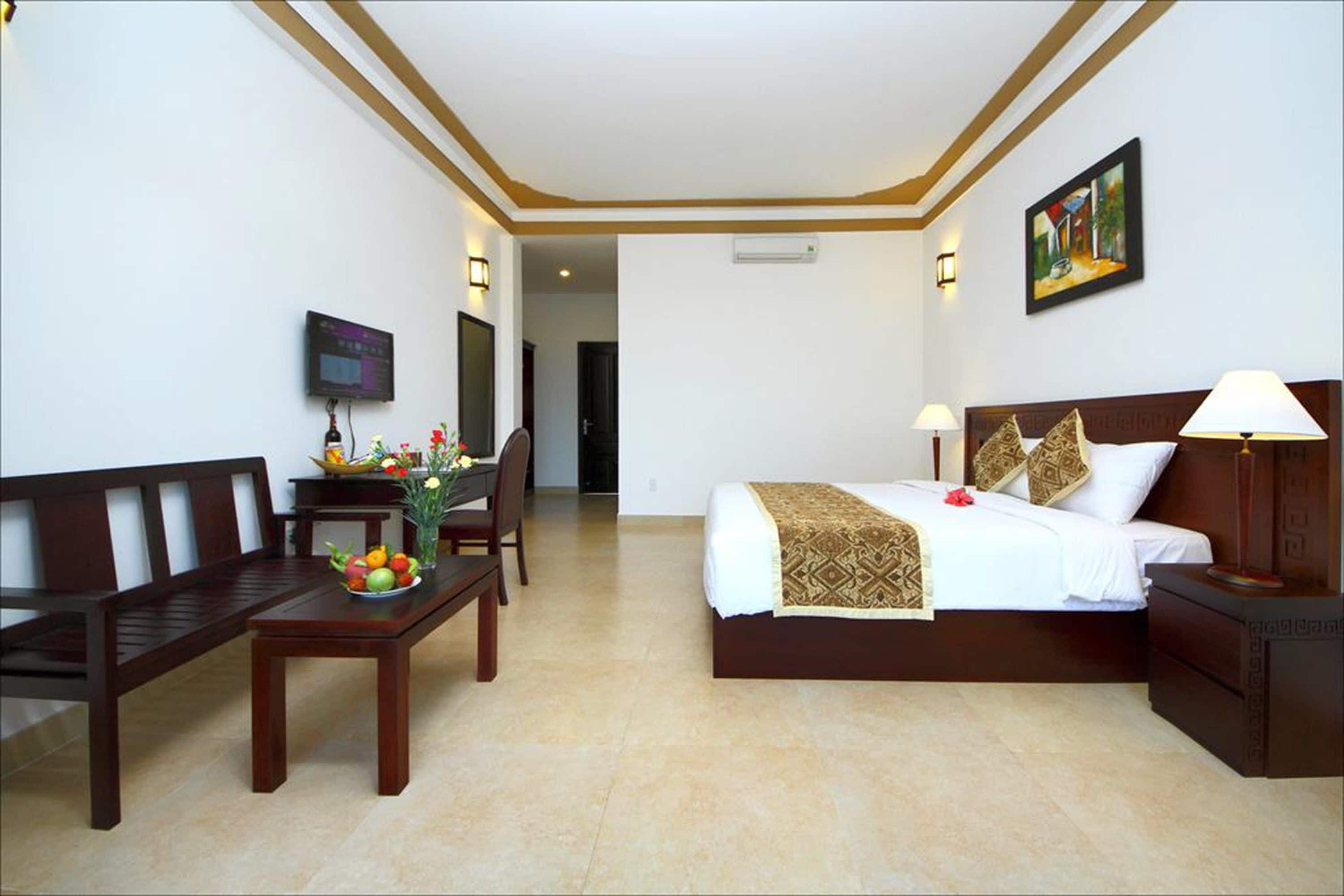 Camera d'albergo con un letto, un comodino, una lampada e una scrivania con sedia e fruttiera.
