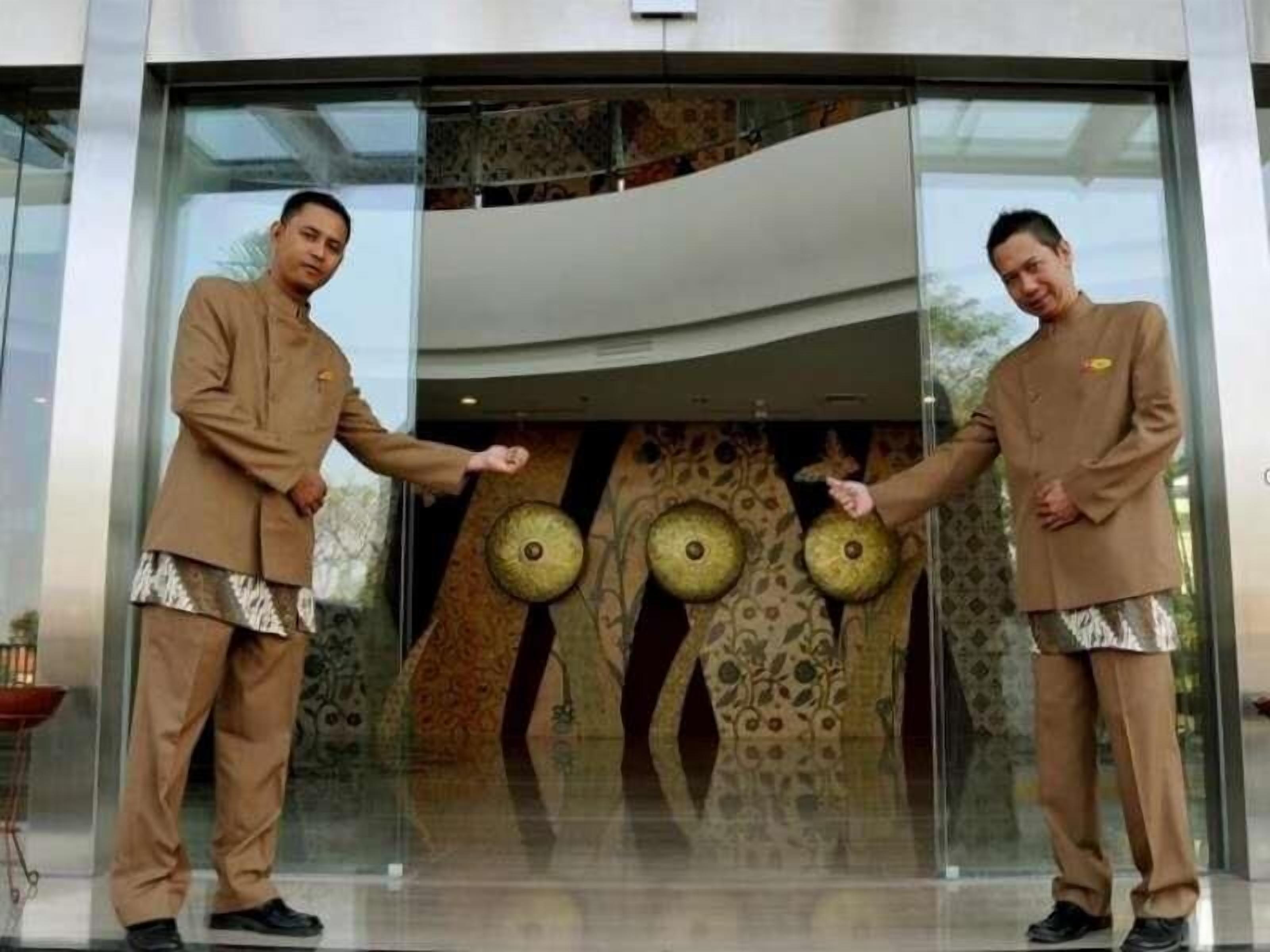 Dos personas con vestimenta similar frente a un edificio moderno con amplias puertas de vidrio.