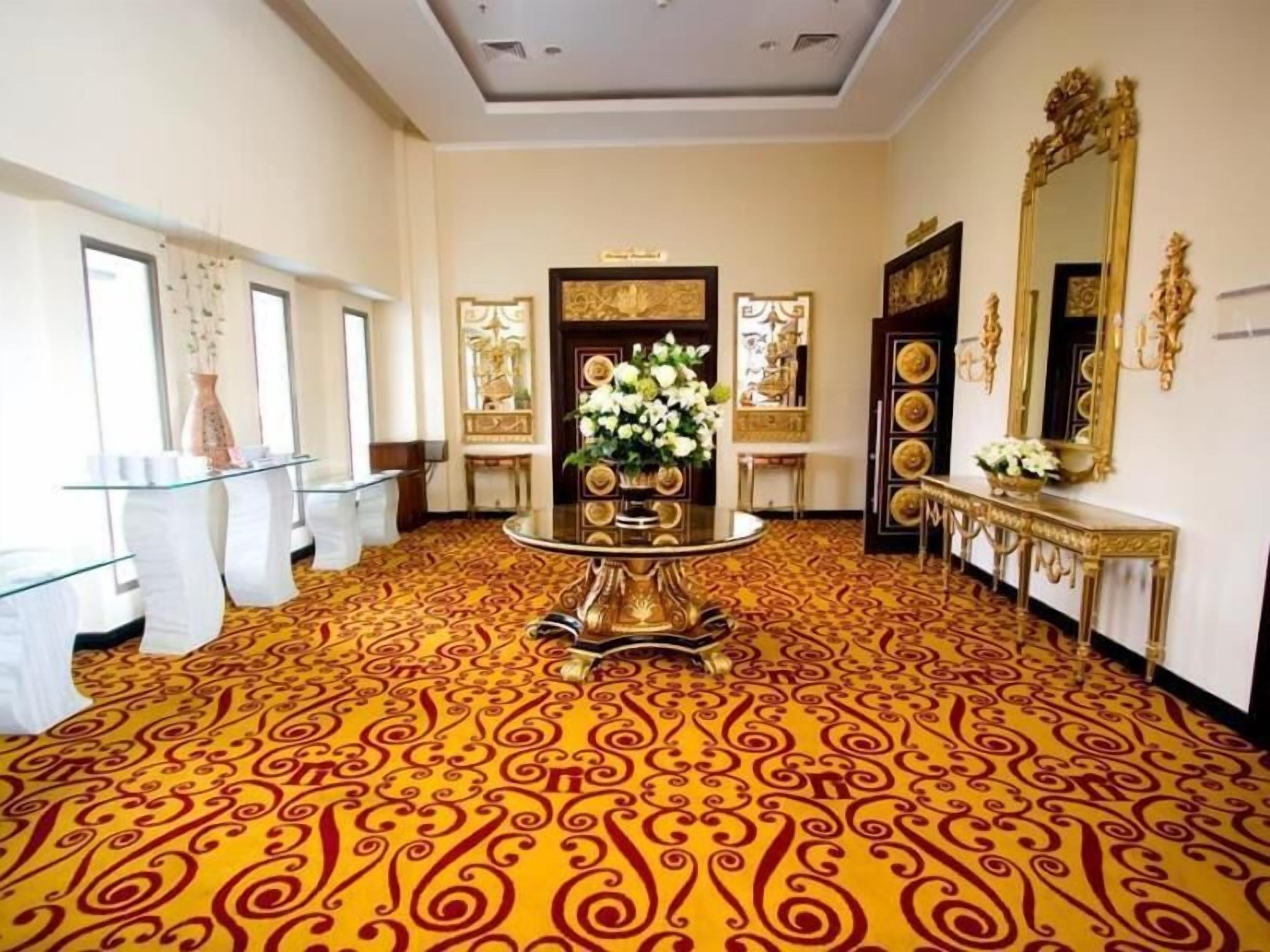 Un elegante vestíbulo de hotel con decoración ornamentada, alfombra estampada y un arreglo floral central.