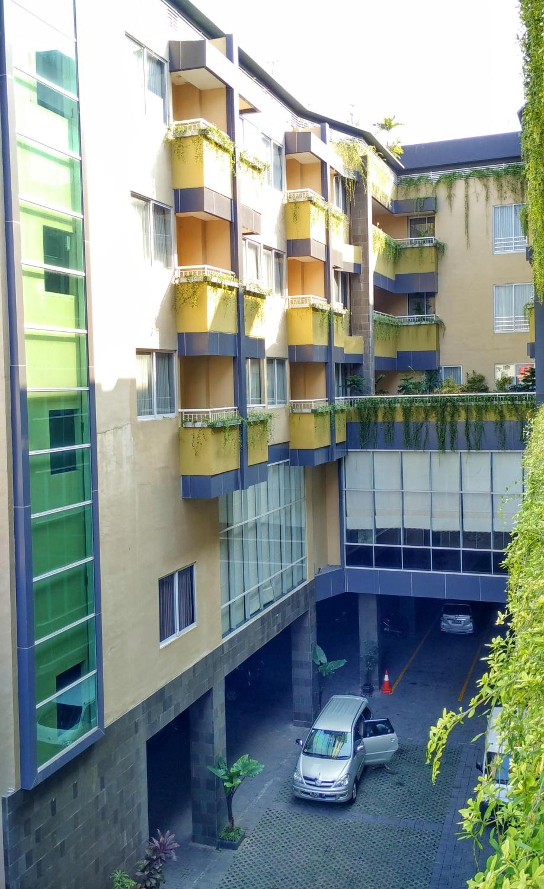 A multi-story building with balconies, a covered parking area, and a car parked in the lot.