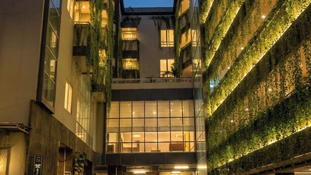 Un edificio moderno de varios pisos, con amplios ventanales y un patio empedrado.