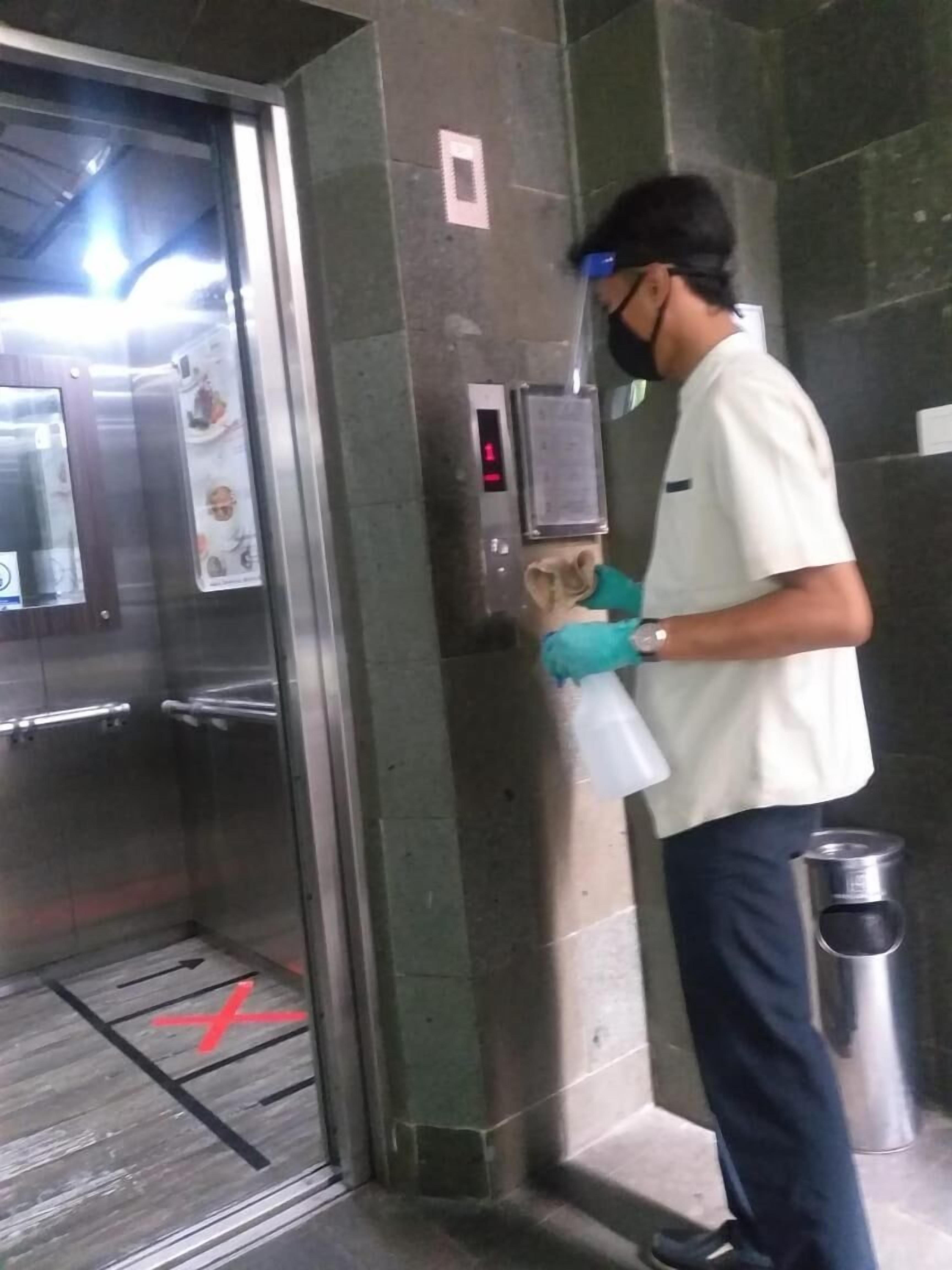 Una persona limpia la puerta de un ascensor de vidrio con un pulverizador y un trapo.