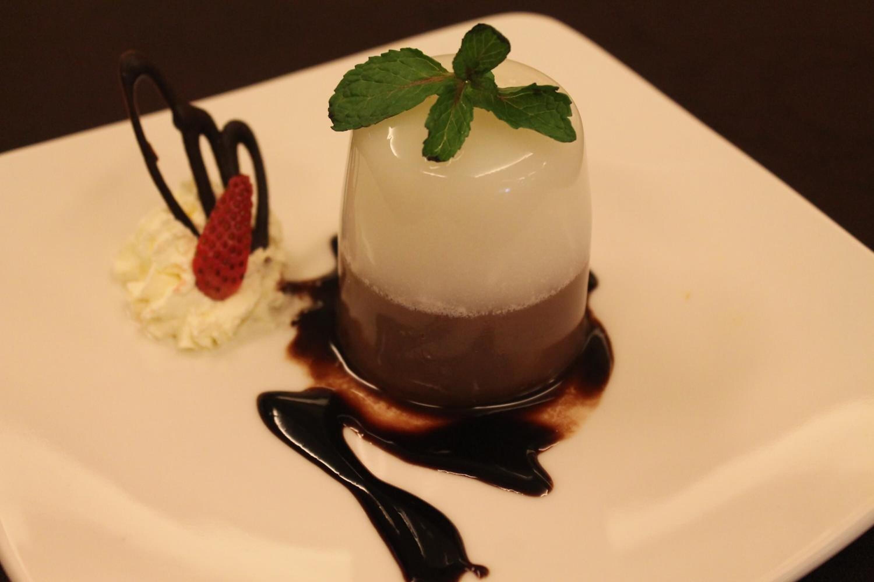 A dessert on a white plate with a mint garnish and chocolate drizzle.