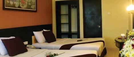 A hotel room with two beds, a painting on the wall, an air conditioning unit, and a small table with a vase of flowers and a candle.
