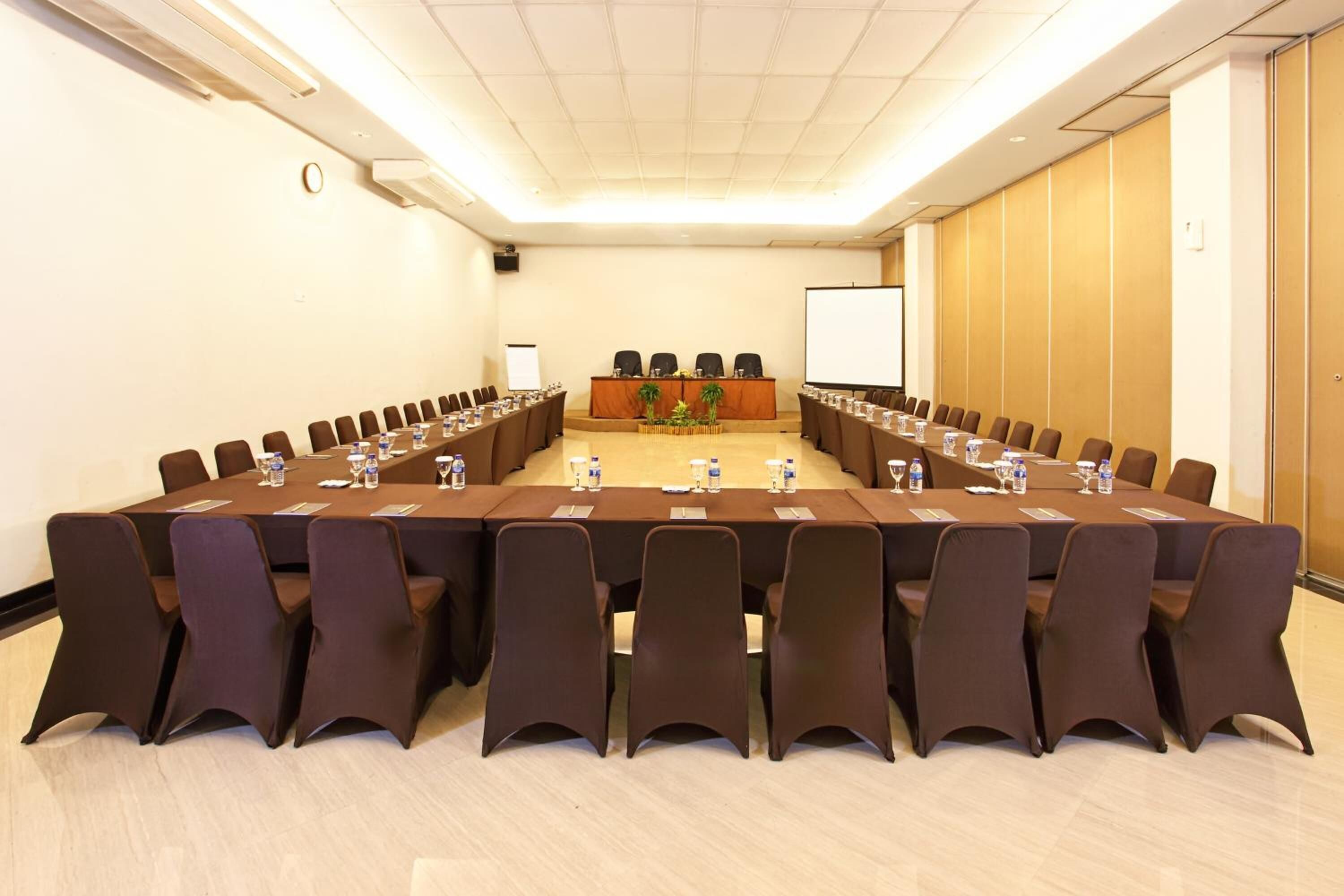 A conference room with a long table, chairs, a projector screen, and a podium.