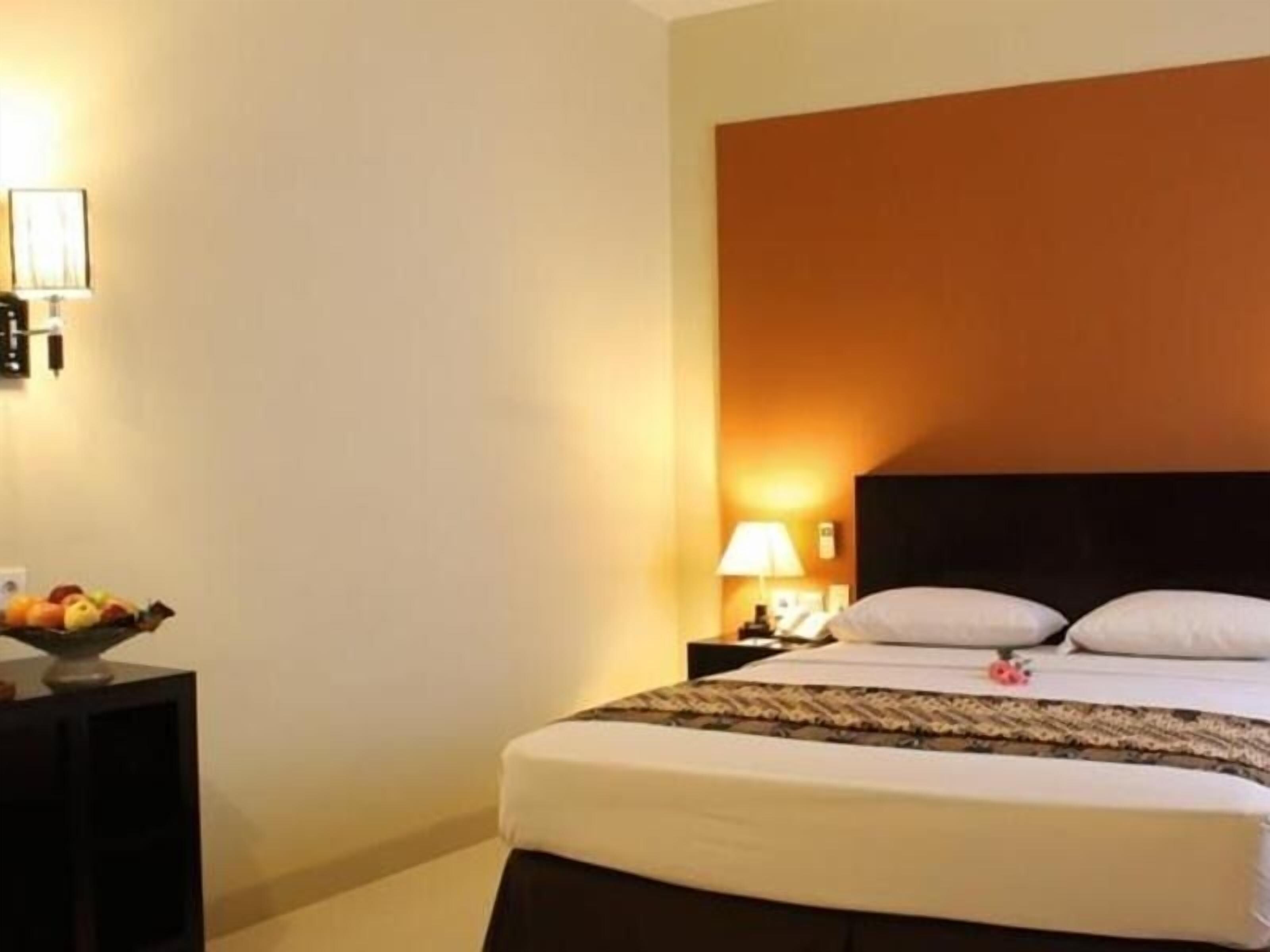 A hotel room with a bed, a nightstand with a lamp, and a fruit bowl.