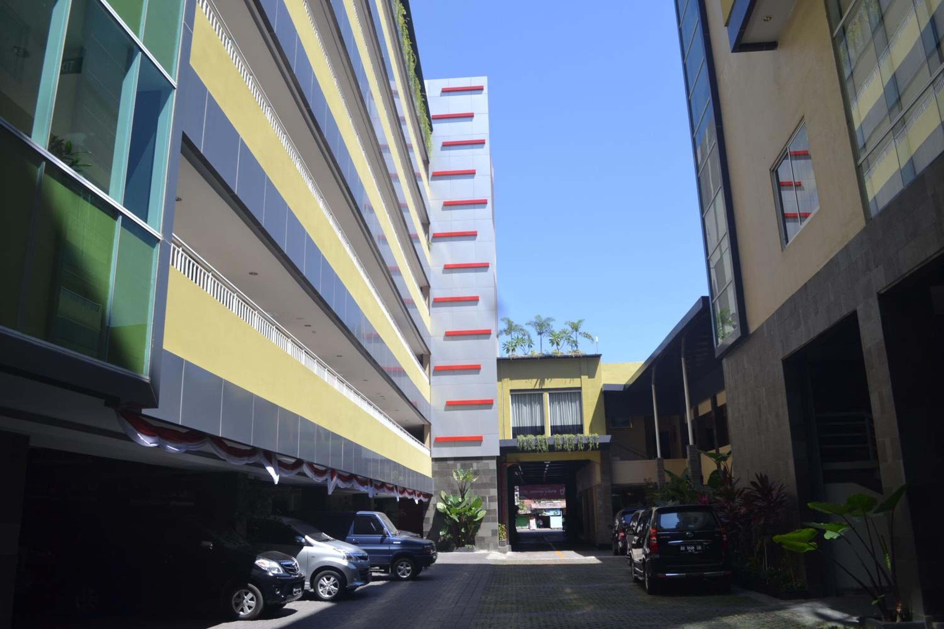 A multi-story building with a modern design, featuring a mix of glass and concrete facades. There are several parked cars in front of the building, and a clear blue sky above.