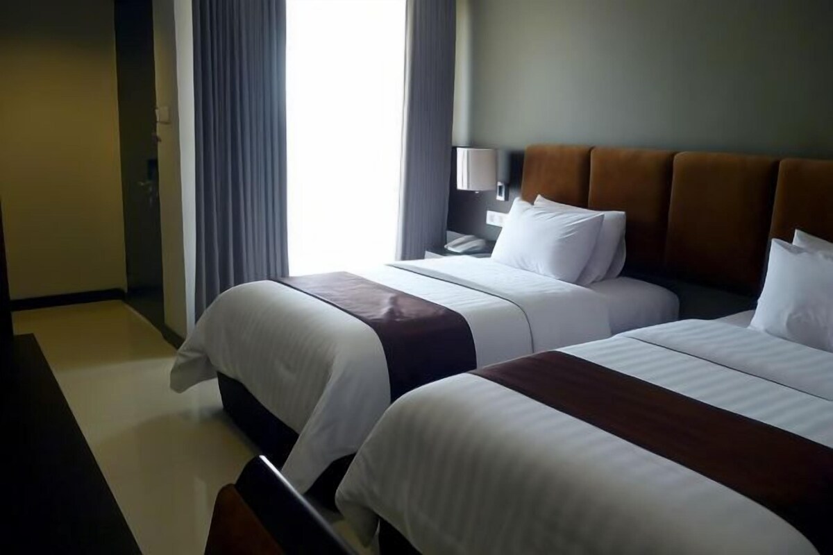 Een hotelkamer met twee bedden, een nachtkastje, een lamp en een raam met gordijnen.