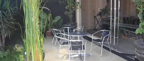 An outdoor patio area with metal chairs and tables, surrounded by potted plants and a piano.