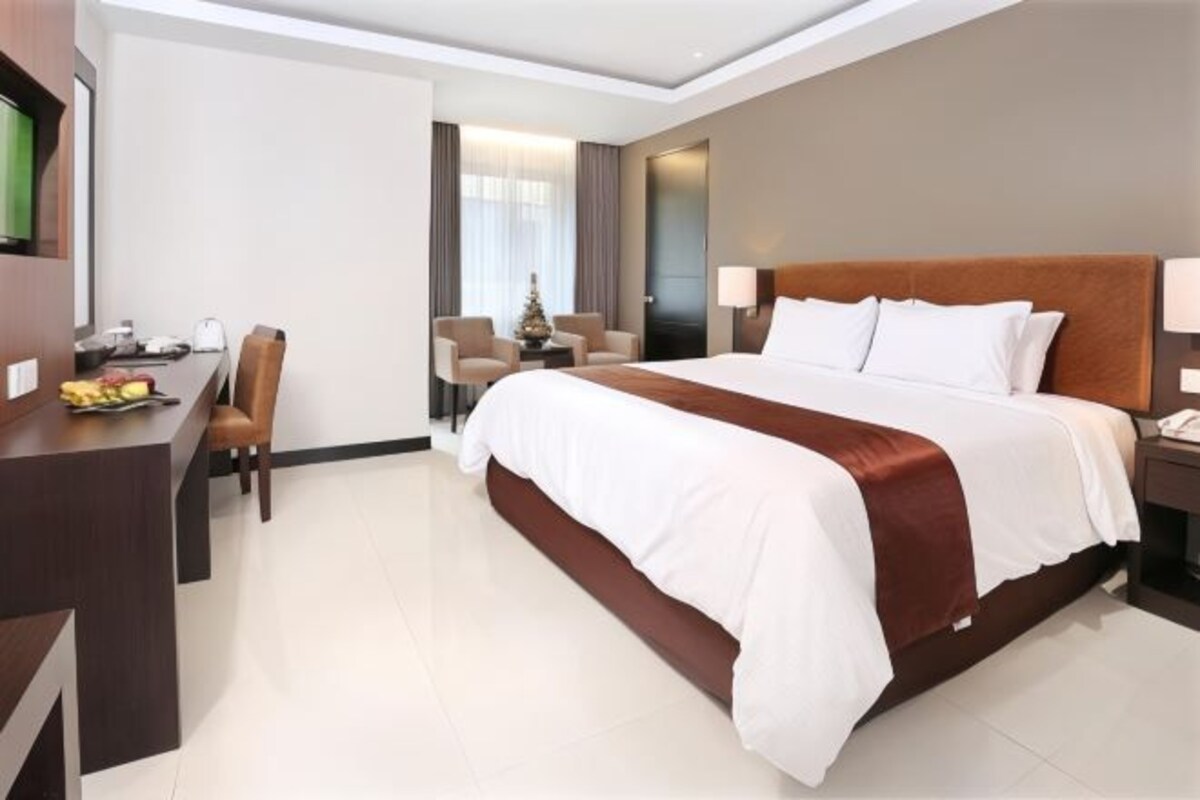 Een hotelkamer met een groot bed, een bureau met stoel, een klein tafeltje met een kerstboom en een televisie aan de muur.