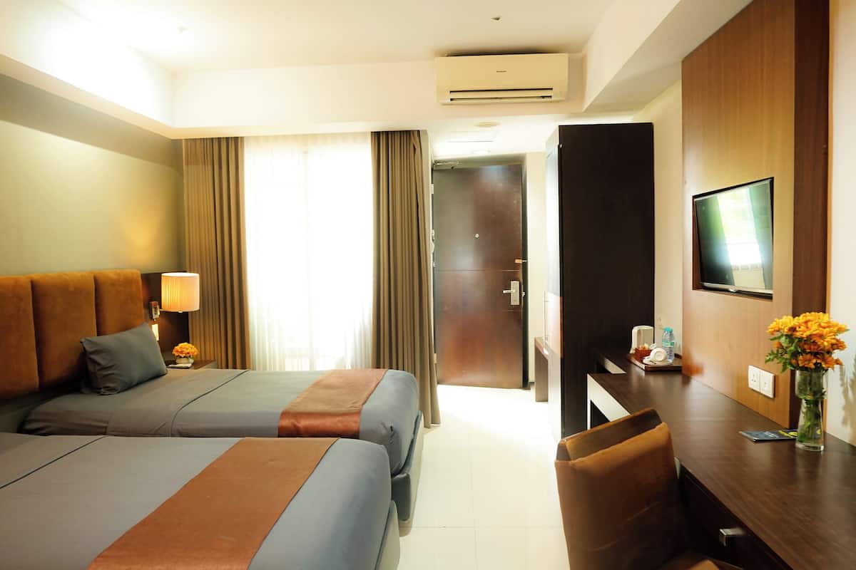 Habitación de hotel con dos camas, un escritorio, un televisor y un florero con flores.