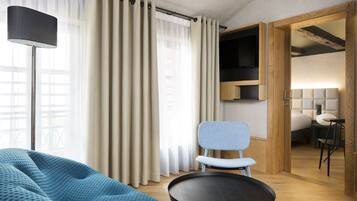 Una habitación de hotel moderna con una cama grande, un sofá azul, una mesa redonda y un televisor sobre una estantería de madera.