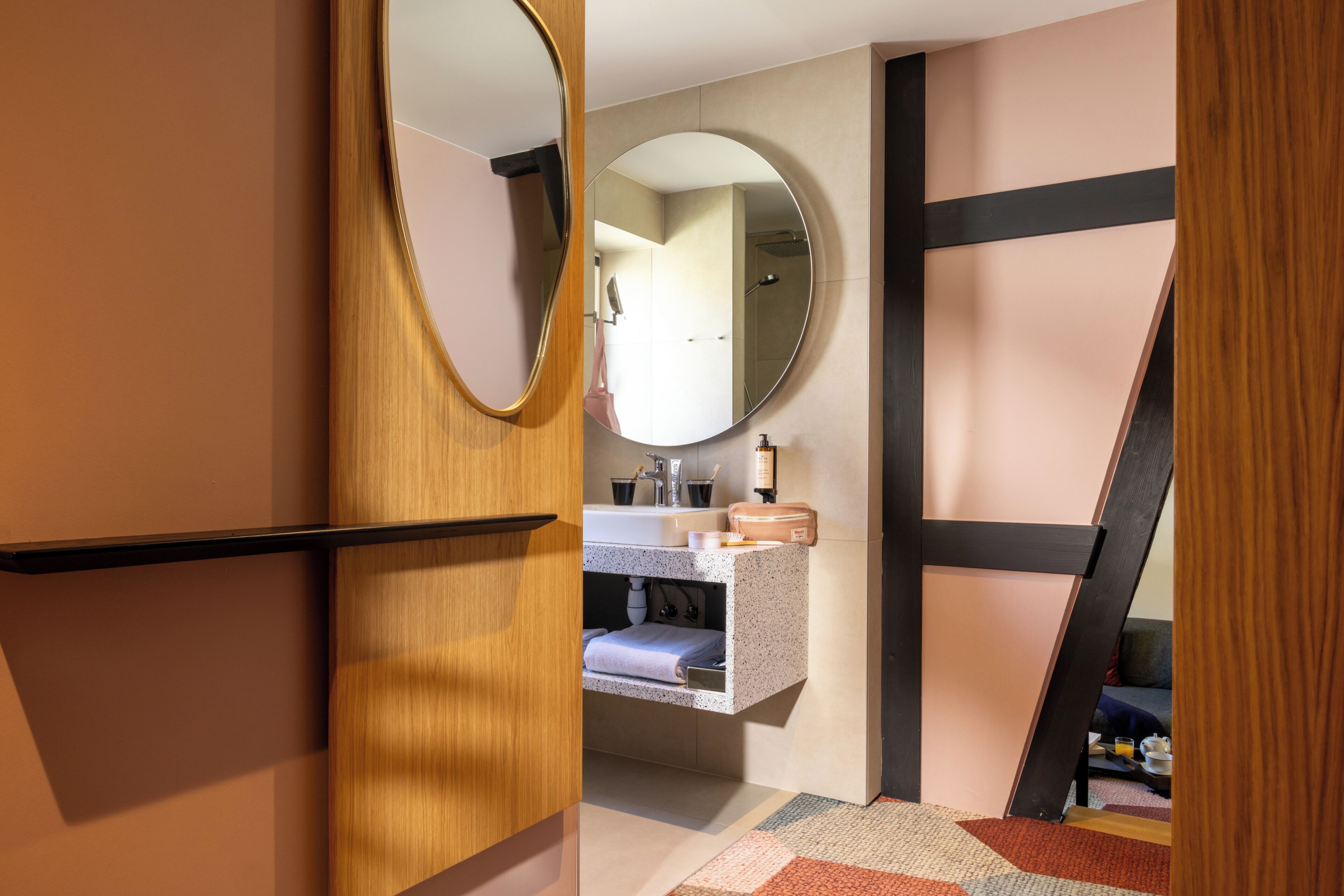 Un baño moderno con tocador de madera, un espejo redondo, lavamanos integrado y un perchero para toallas.