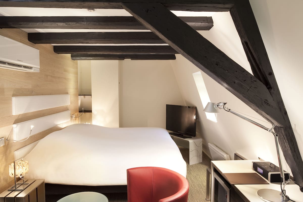 Ein Hotelzimmer mit einem großen Bett, einem Fernseher, einem Schreibtisch mit Lampe und einem roten Sessel.