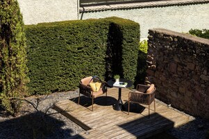 Un patio al aire libre con una terraza de madera, dos sillas de mimbre, una pequeña mesa redonda y una planta en maceta.