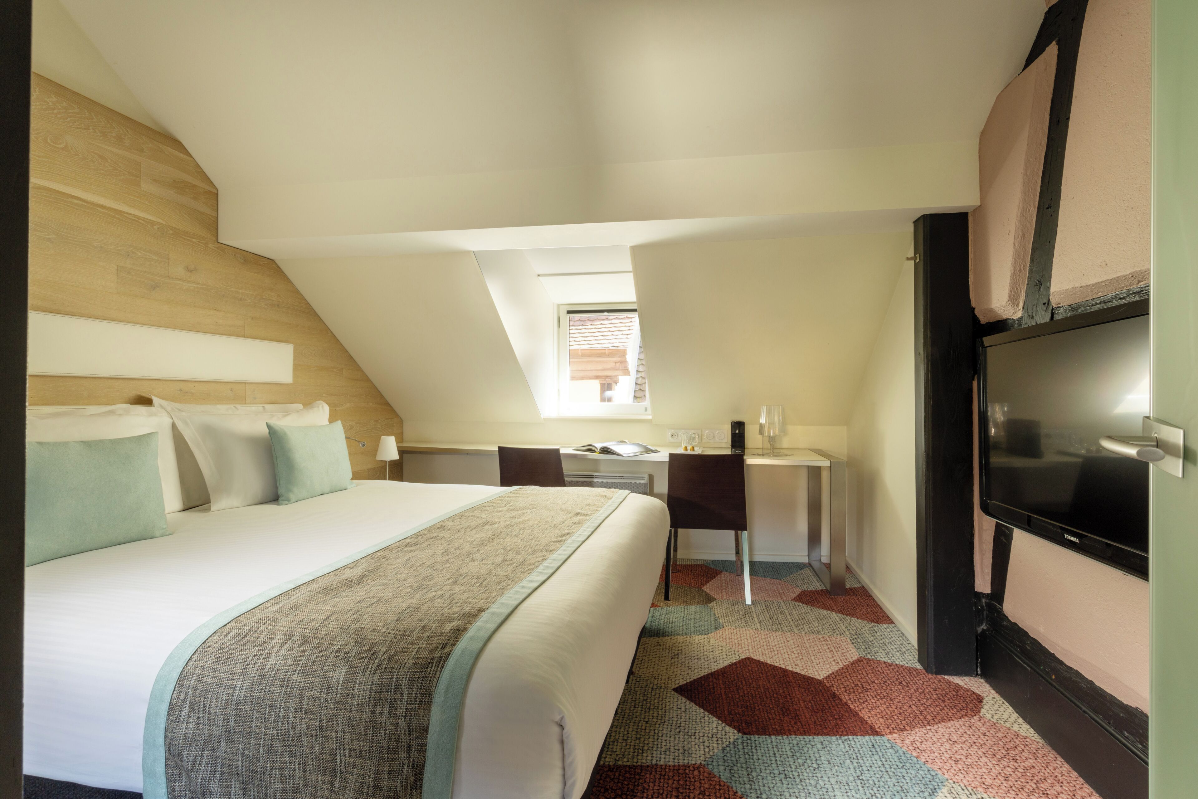 Una habitación de hotel con cama, escritorio, silla, televisor y ventana.