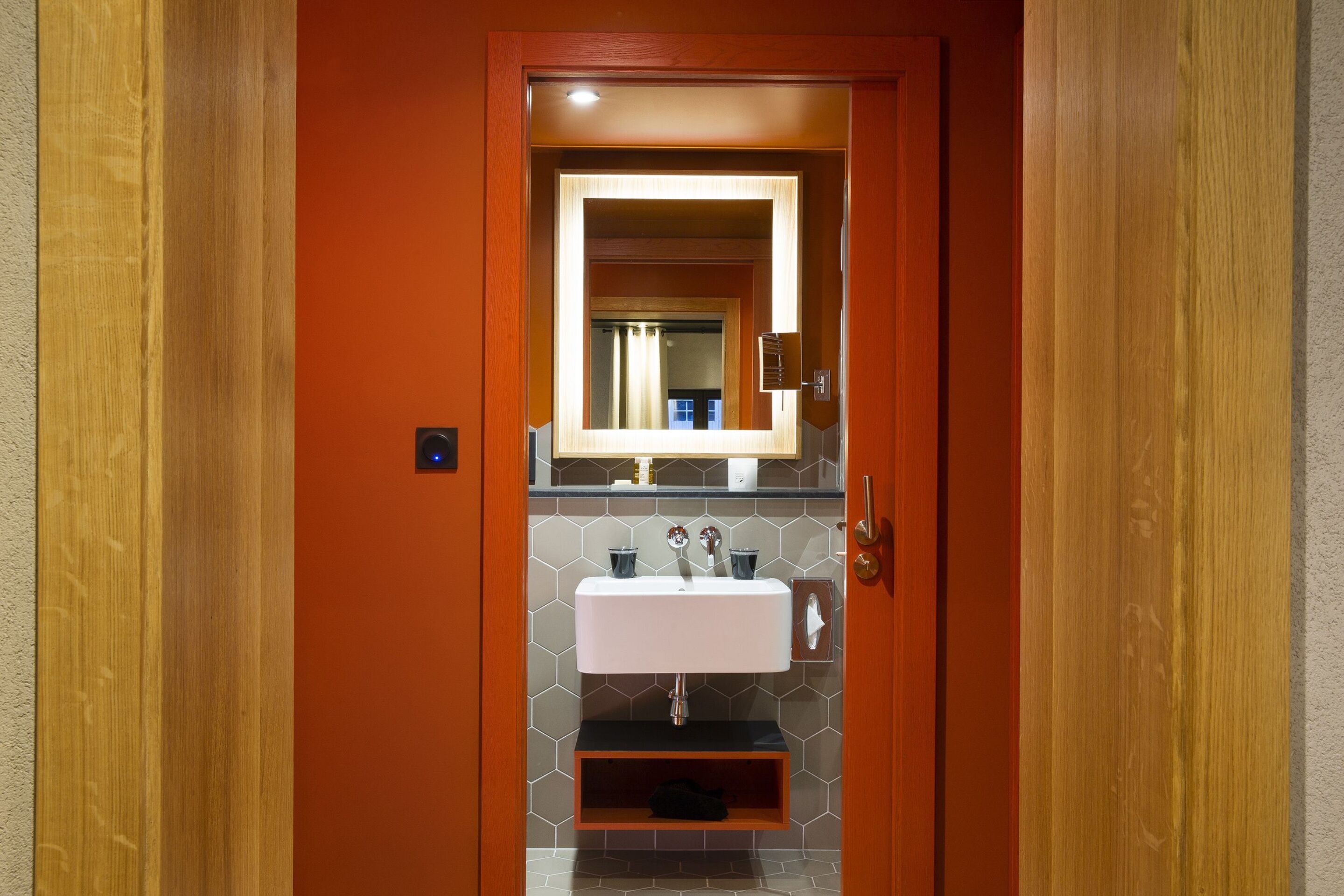 Un baño con un lavamanos blanco, un espejo y una puerta de madera.