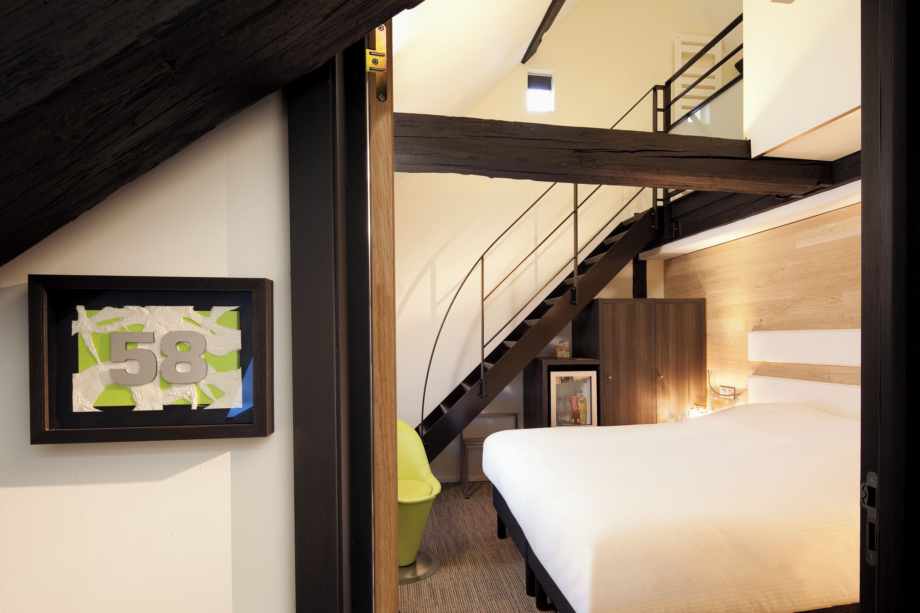 A bedroom with a bed, a framed number sign, a staircase, and a small window.