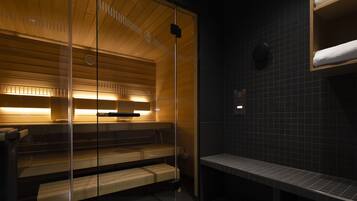 A sauna with wooden benches and glass walls, a tiled wall, and a bench with towels.
