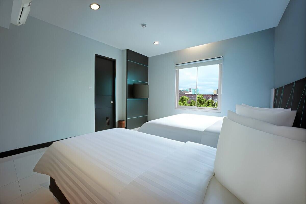 A modern hotel room with a large bed, a wardrobe, a window with a view, and a ceiling-mounted air conditioning unit.