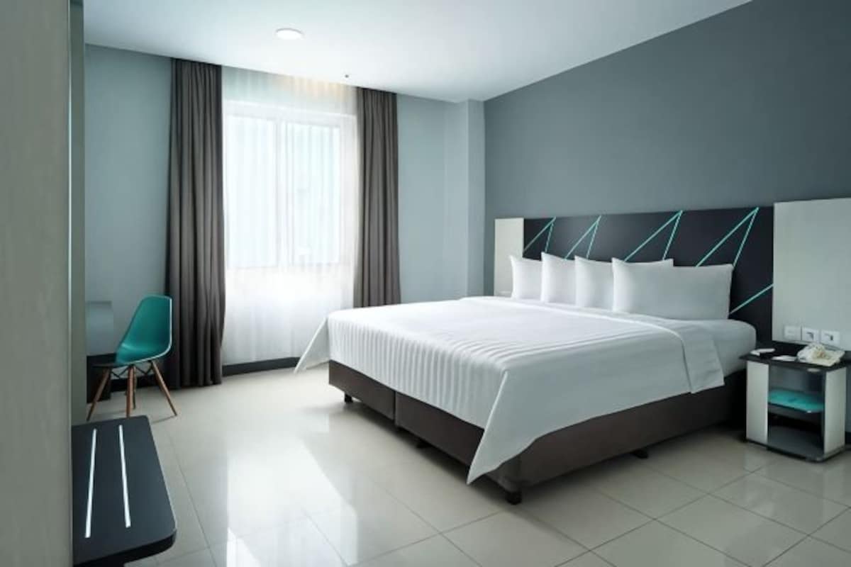 Una habitación de hotel moderna con una cama grande, un escritorio, una silla y una mesita de noche.