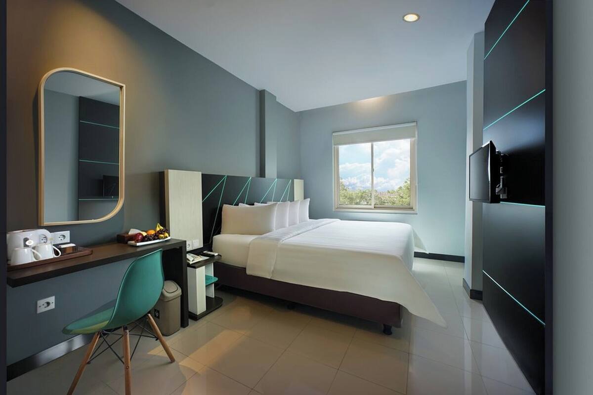 A modern hotel room with a large bed, a desk with a chair, a TV, and a window with a view.