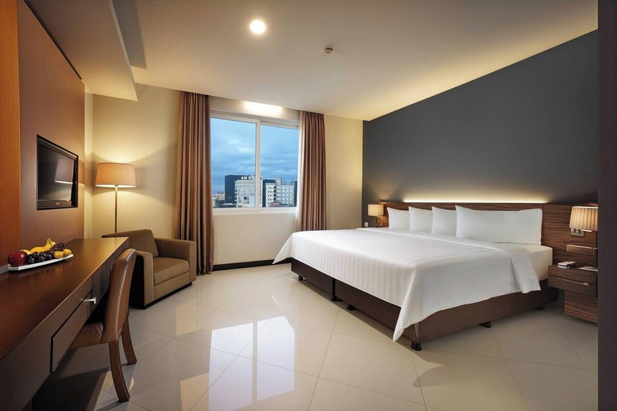 A hotel room with a large bed, a desk with a chair, a TV, and a window with curtains.