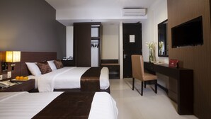 Une chambre d’hôtel avec deux lits, un bureau, une chaise, une télévision et une salle de bain visible à travers une porte ouverte.