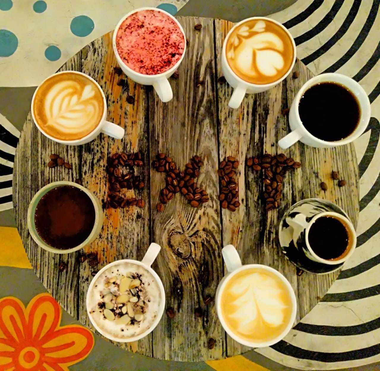 A wooden table with eight cups of coffee and coffee beans arranged in a circle.