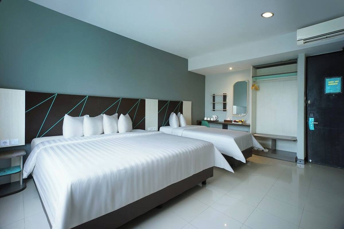 A hotel room with two beds, a desk, a chair, a mirror, and an air conditioning unit.